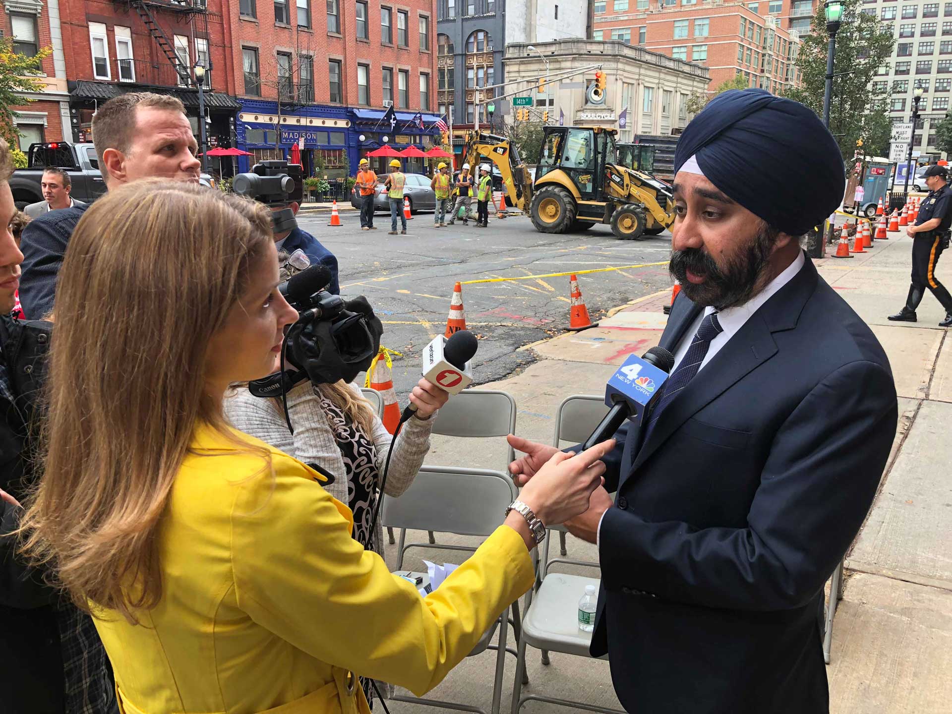 Jen in the field interviewing a man in a suit and tie, wearing a turban